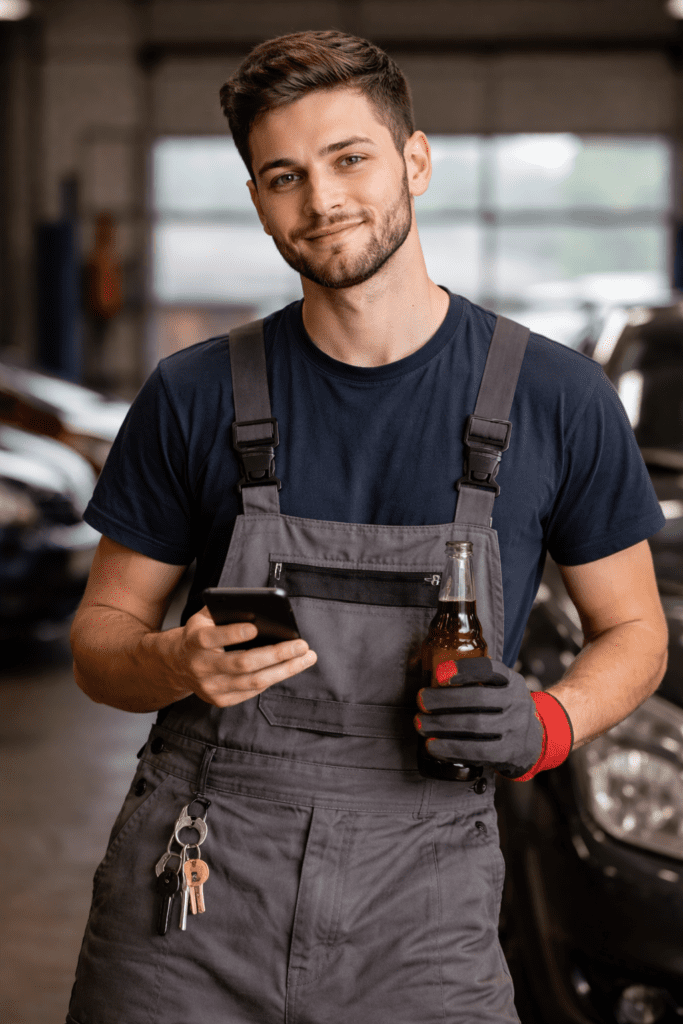 Single millennial automotive technician checking his phone while at work, representing common budgeting challenges with discretionary spending.