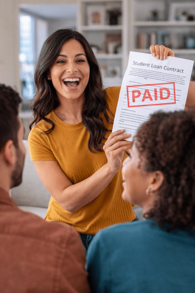 Millennial woman smiling and holding a student loan contract marked “Paid” while showing it to friends in a living room.